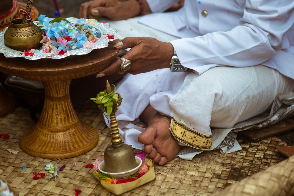 A priest's hands ring a bell above offerings and flower petals.