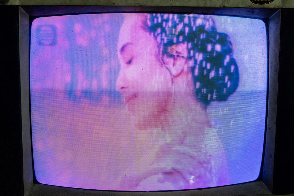 A television close-up of a woman in profile, the screen washed pink.