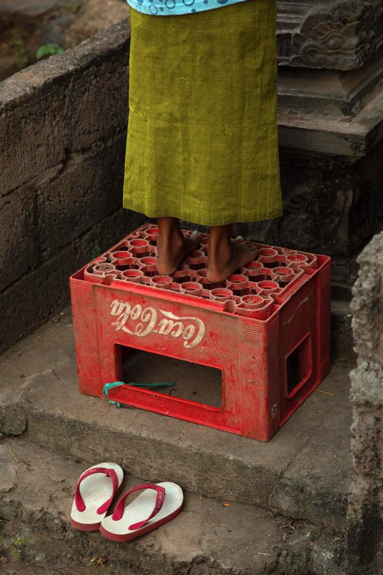 A person in a green sarong stands barefoot on a red crate.
