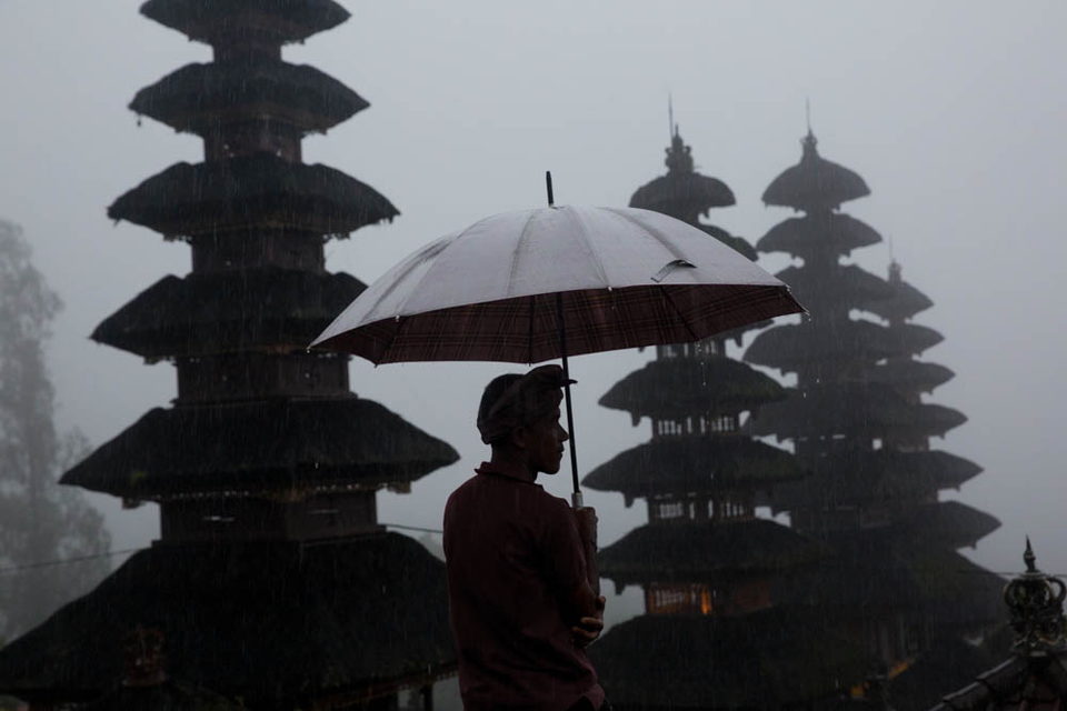 A man with an umbrella stands before temple spires in rain and mist.