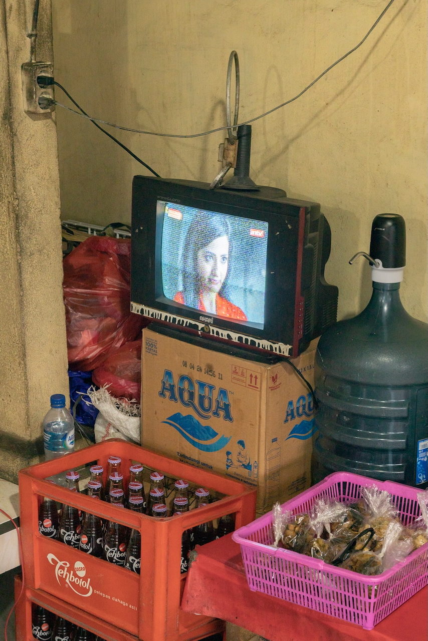 A television atop stacked water boxes and crates of bottles.