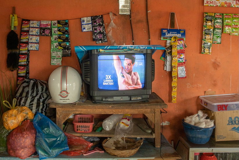 A television on a wooden stand beside a helmet and hanging sachets.