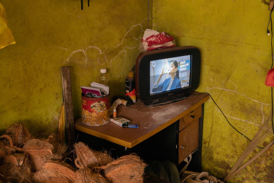 A television on a wooden desk beside sacks and jars.