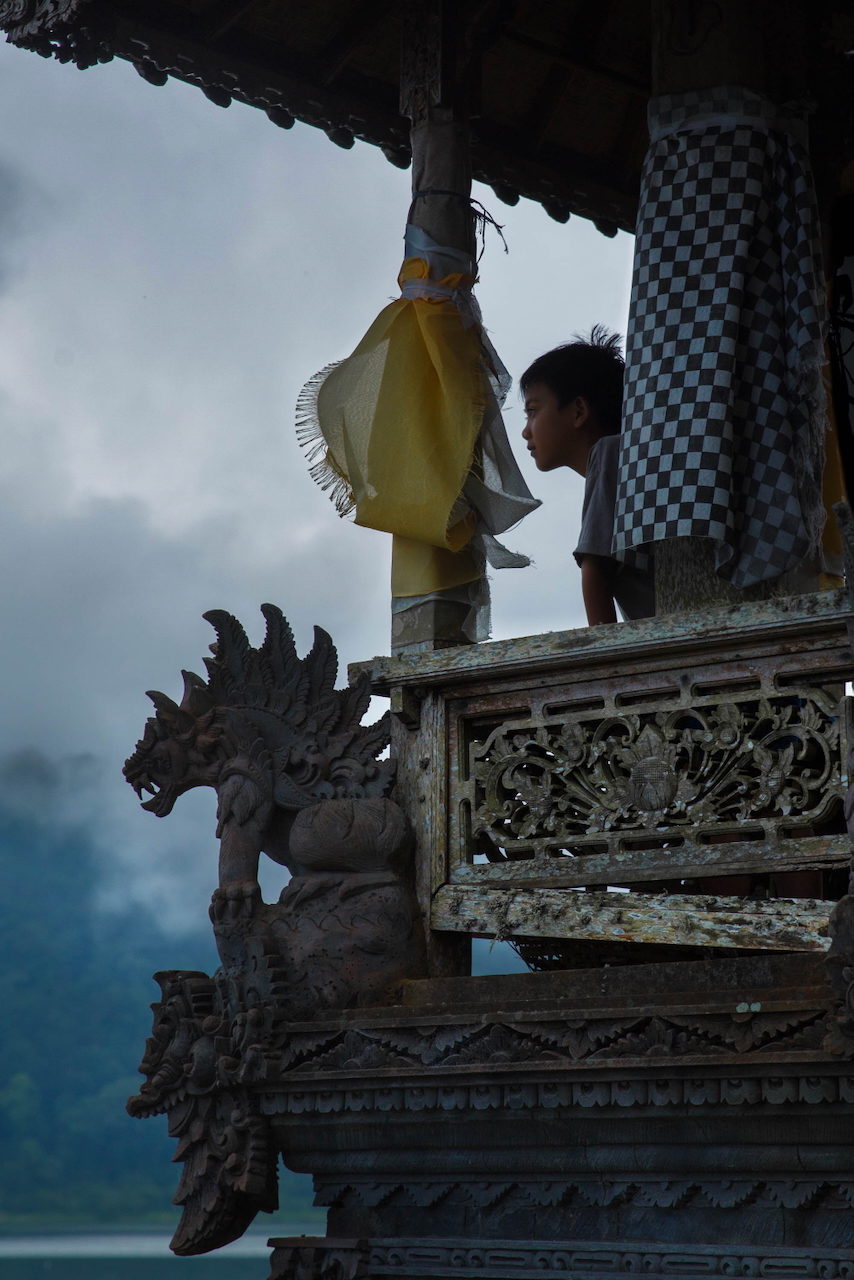 A boy stands beside a carved shrine and a yellow banner.