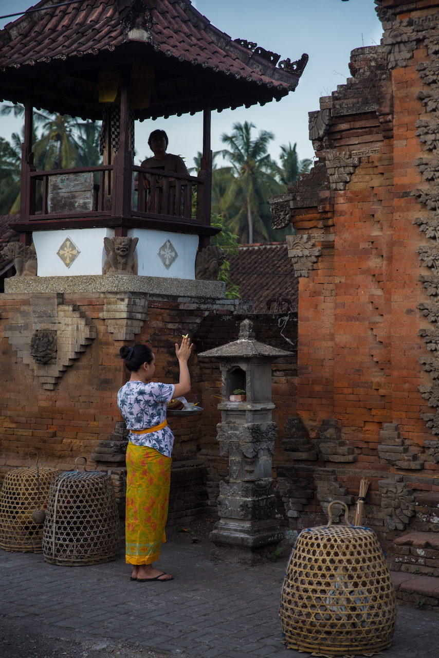 A woman makes an offering at a brick shrine in a family compound.