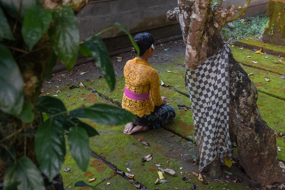 A woman sits on wet ground beside a checked-cloth shrine.