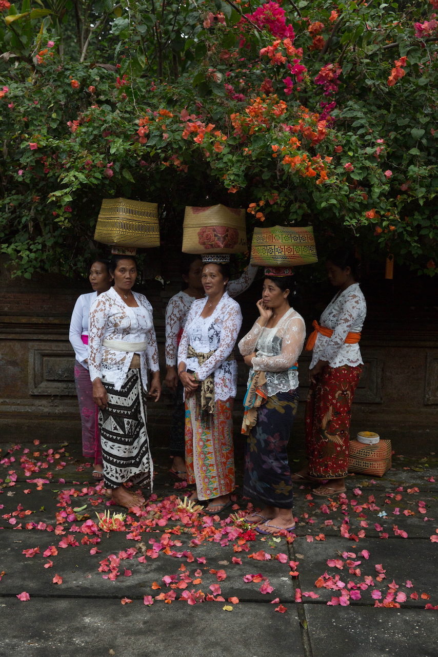 Women in lace carry tiered offerings beneath a bougainvillea.