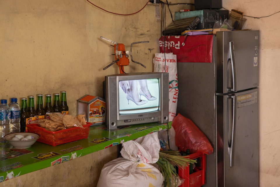 A television on a green shelf beside a fridge and sacks.