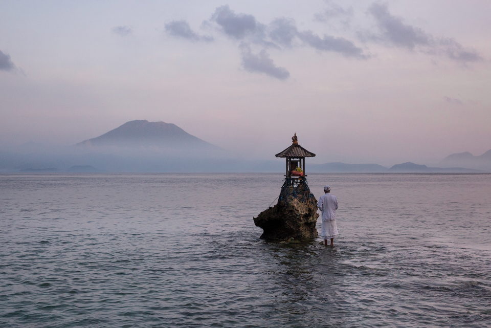 A small shrine on a rock in still water at dusk, a figure standing beside it.
