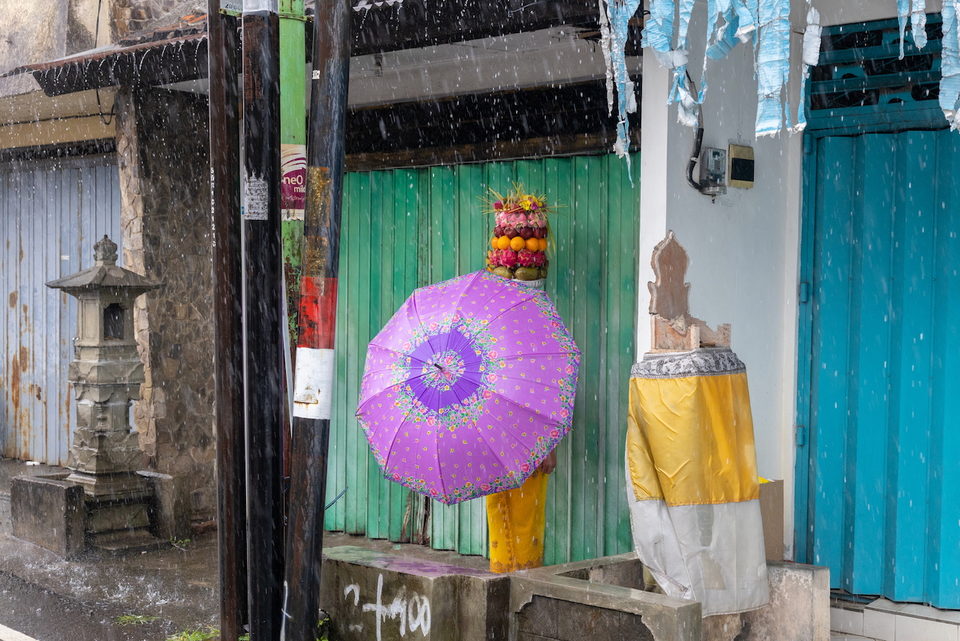 A pink parasol and offerings at a green gate in the rain.