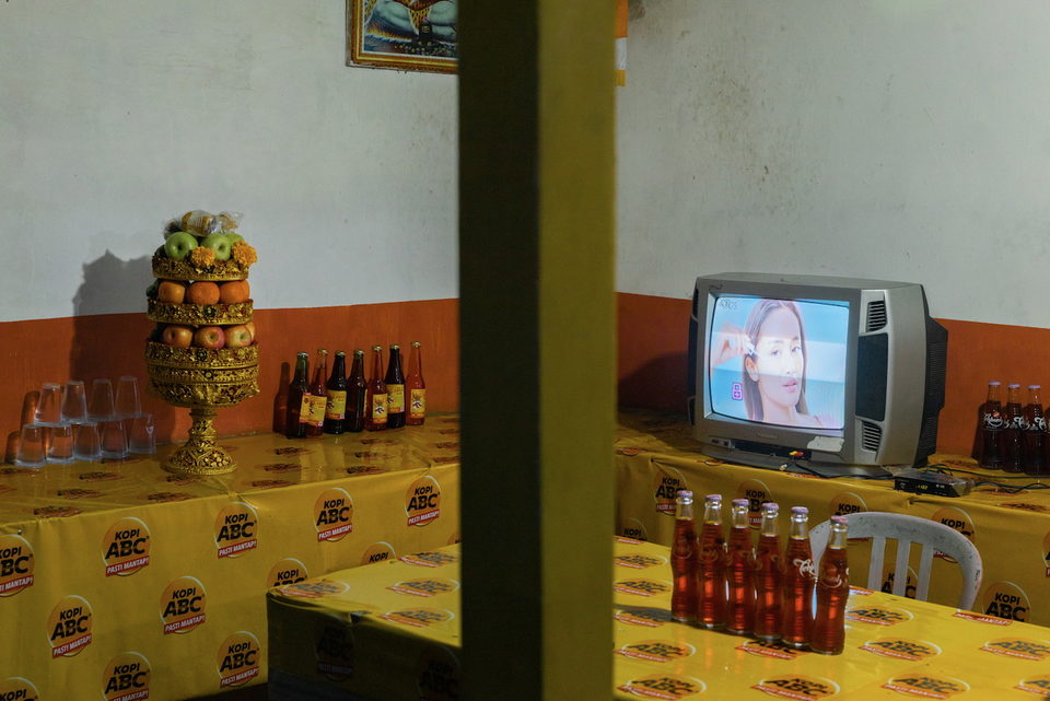 A television on a counter of yellow packets and bottles.